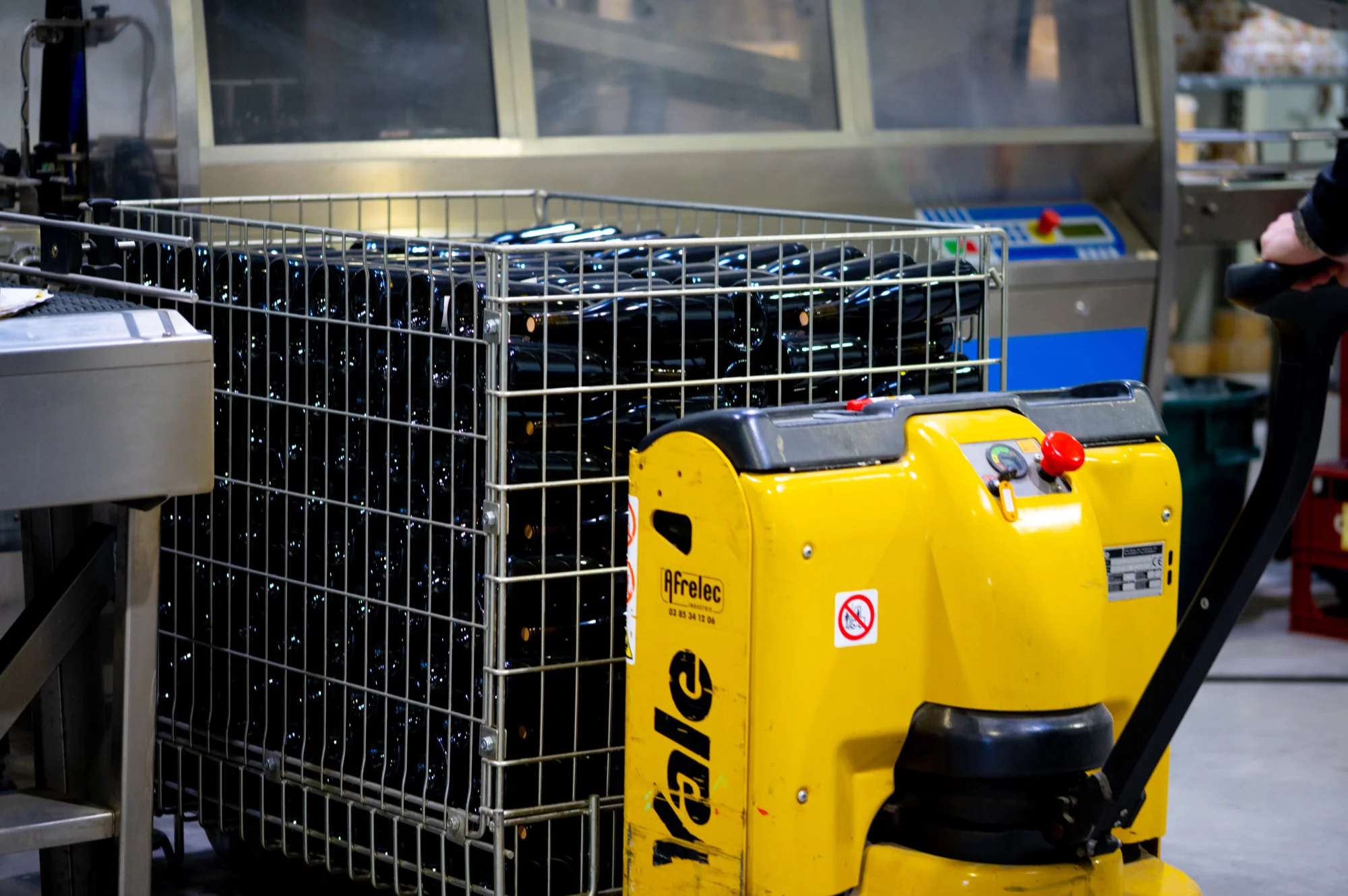 Caisse de bouteilles déplacée au transpalette électrique dans l'atelier
